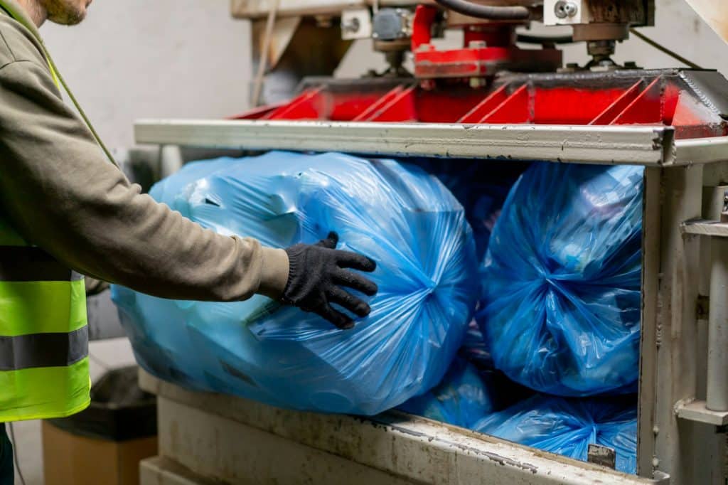 a recycling plant employee putting bags of garbage into special press machine for waste disposal