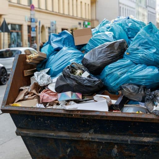 Big metal overloaded dumpster skip container full of plastic trash litter bags near residential